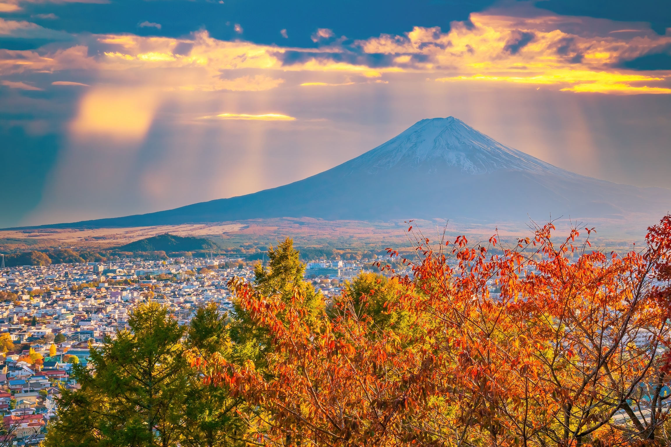 Mount Fuji in Japan. Japanese city foot of volcano. Autumnal Japan. Landscape of Fujikawaguchiko city from afar. Japanese city in autumn morning. Tour Japan. Fuji volcano illuminated by rays of sun