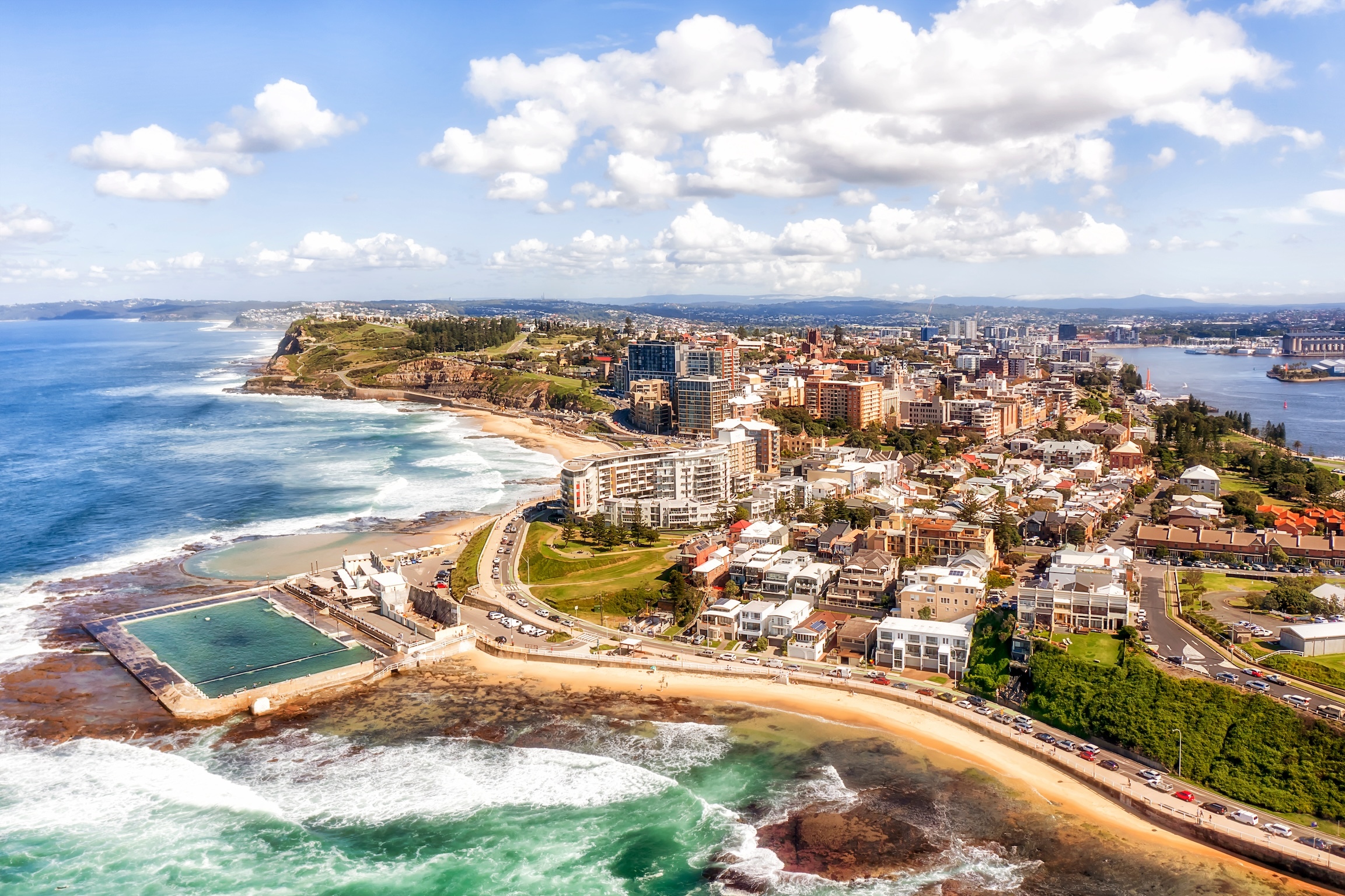 Panorama of Newcastle city on the hills over Hunter river and Pacific ocean with beaches, pool and surfers.