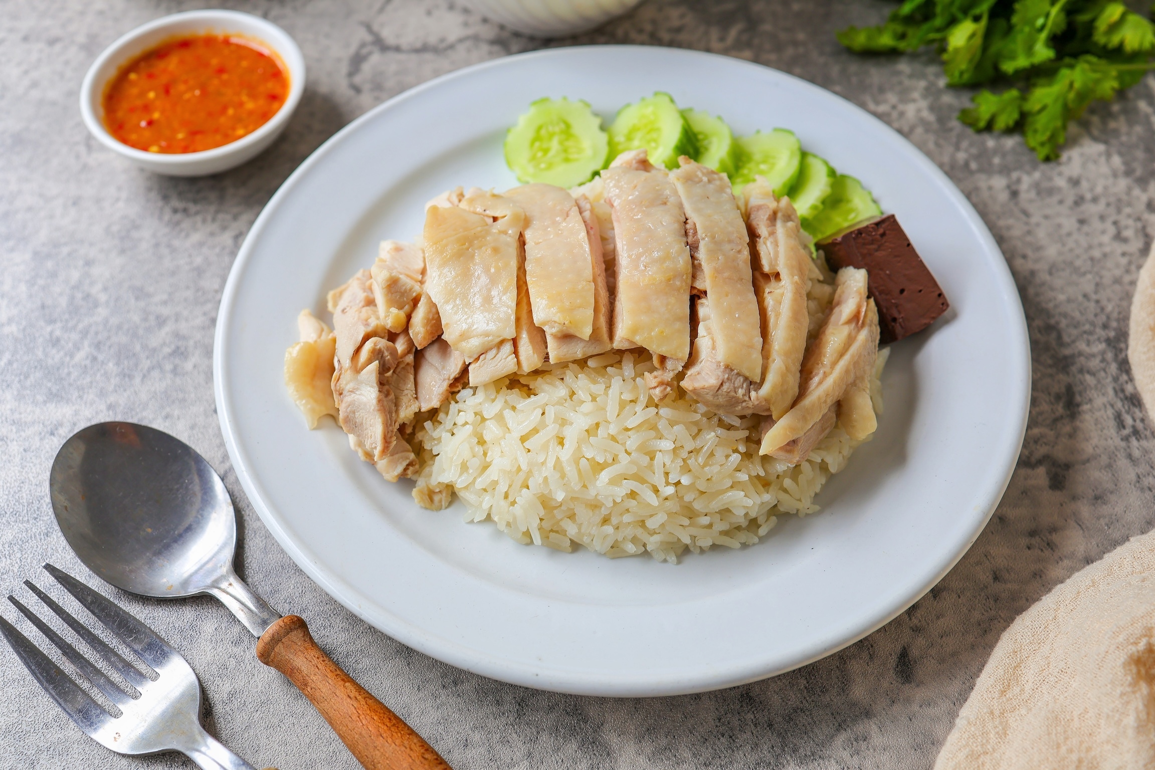 Chicken and rice with coriander and cucumber with sauce and soup in a white plate, hainanese chicken rice, thai called khao man gai, asian food, thai food