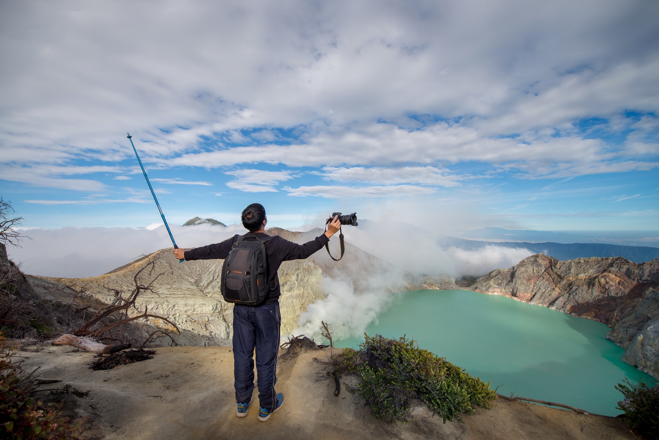 Asian man holding trekking pole and camera on Kawah Ijen volcano summit
